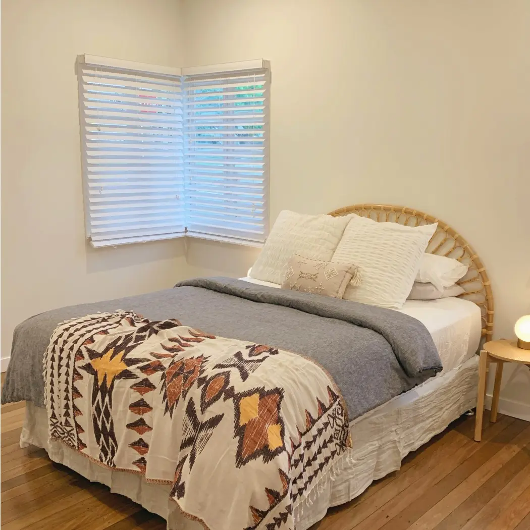 Off-white bedroom with corner window and bed with rattan headboard and white and blue linens