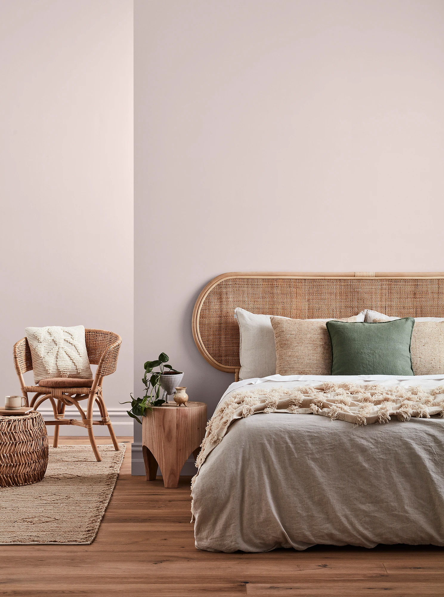 Neutral-coloured bedroom with rattan headboard and chair and neutral linens.