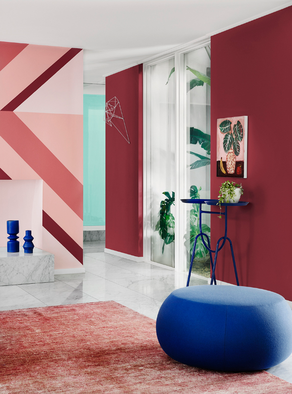 A blue ottoman on a tiled floor with pinkish rug, maroon wall in Dulux Carmen and striped feature wall in Dulux Cuticle Pink, Bombay Pink, Friends and Carmen. Trims and ceiling in Vivid White.