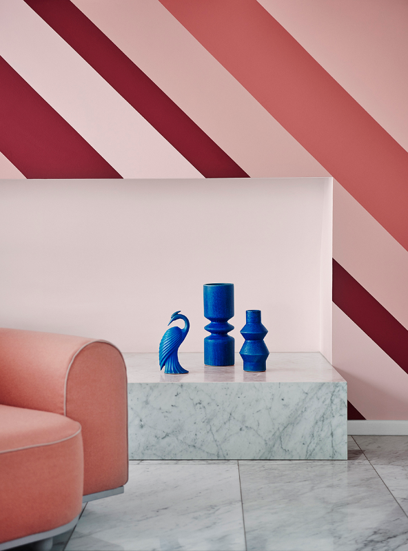 Three blue sculptures on marble fireplace in front of a pink striped wall