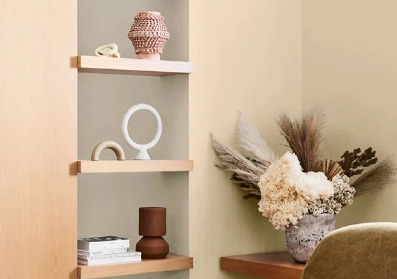 Interior room featuring narrow shelf with candles, books stacked in it and a dried flower arrangement on a bench beside.