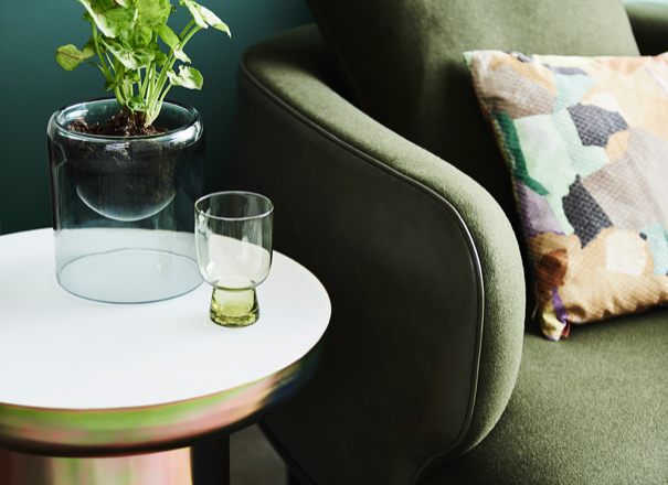 Green fabric armchair with white side table and small plant.