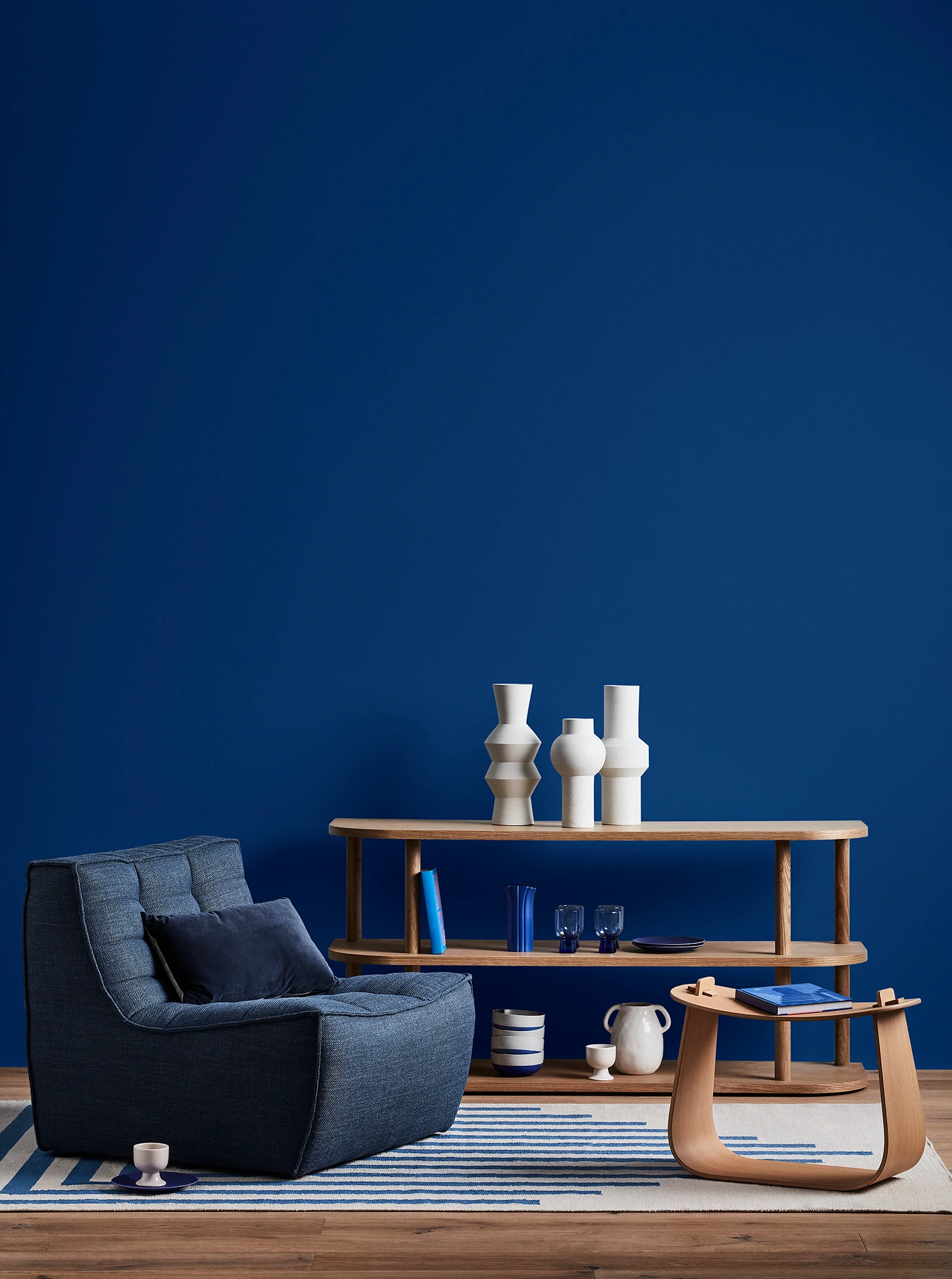 Blue living room with blue armchair, wooden coffee table and shelves with blue and white decor. 