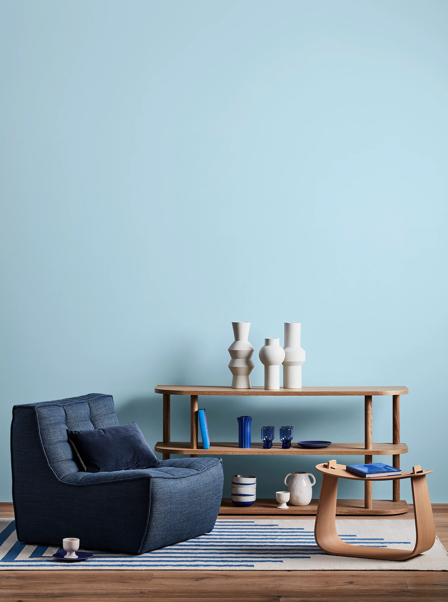 Blue living room with blue armchair, wooden coffee table and shelves with blue and white decor. 