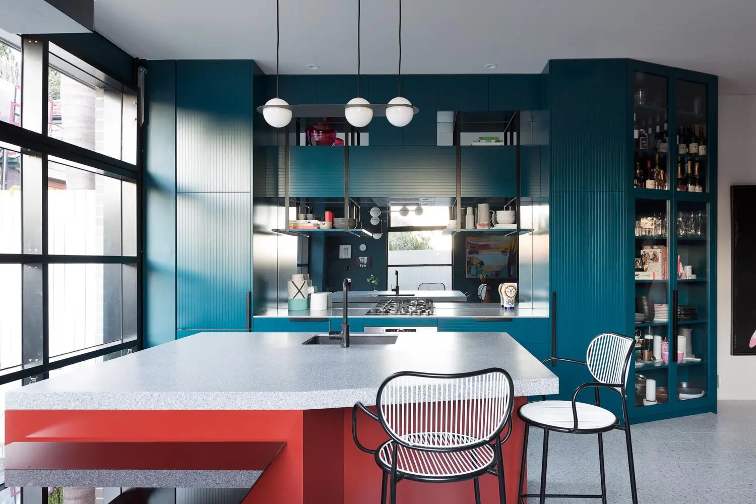 Kitchen with teal cabinets. Island bench with white top and red sides.
