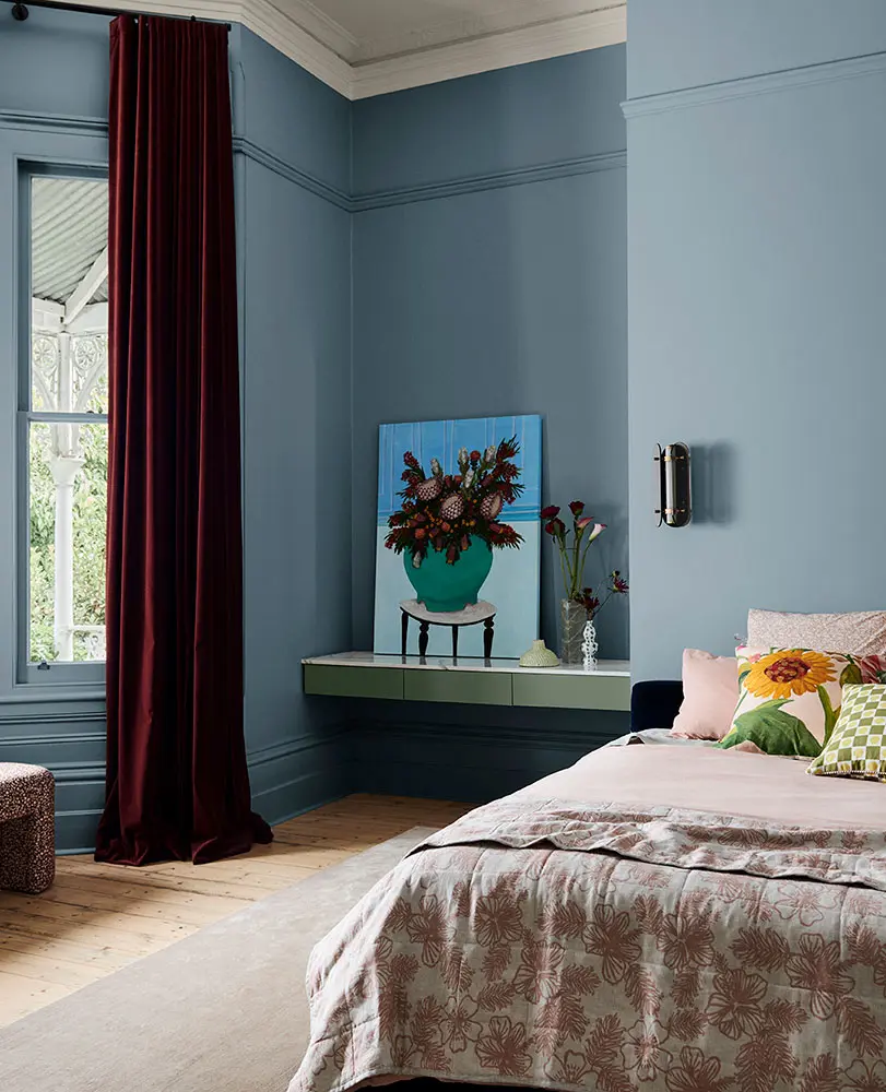 A bedroom with blue walls and a shelf featuring a print of a flower