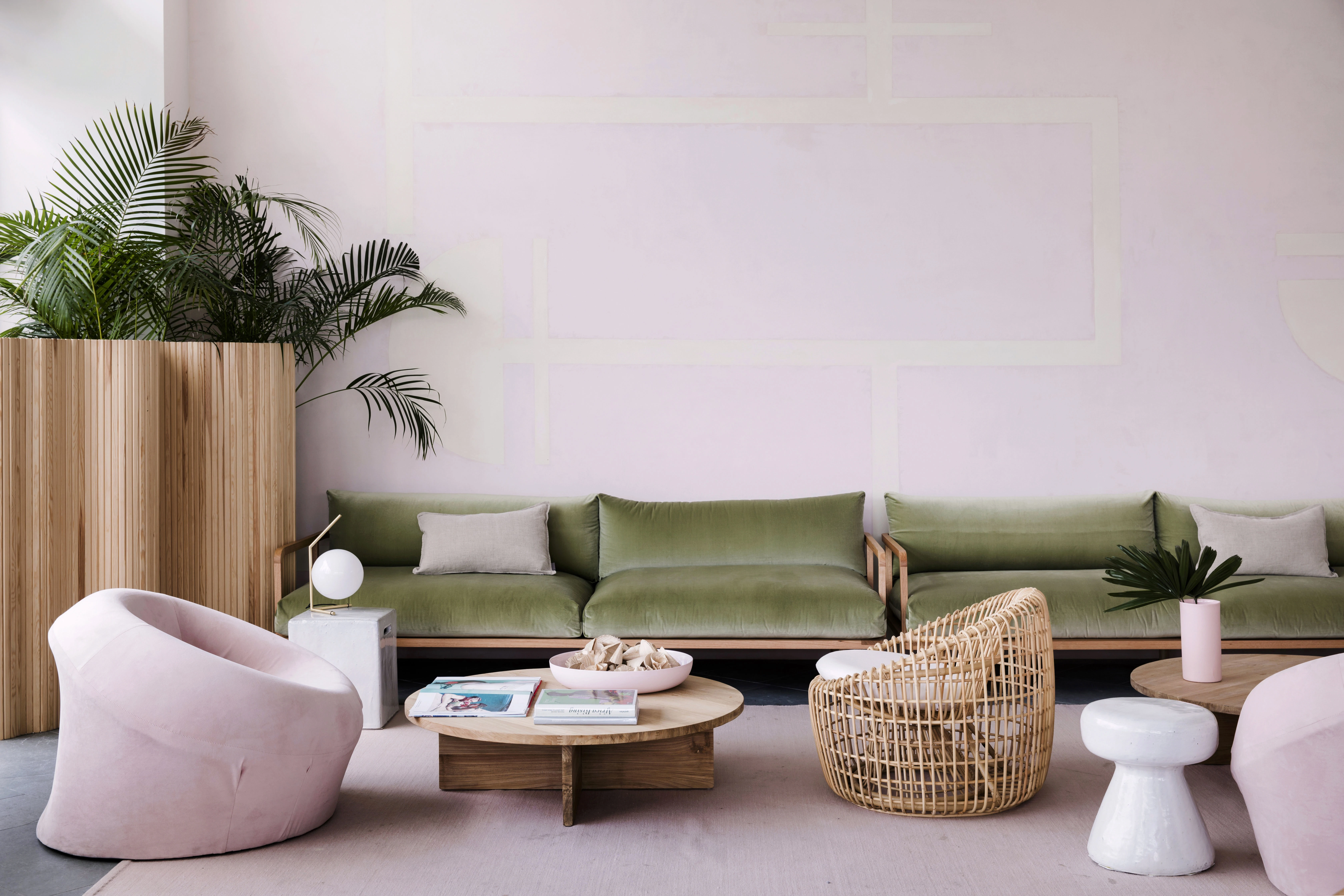 Green velvet couch and pink velvet modern armchairs in hotel lobby with pink walls and palm trees