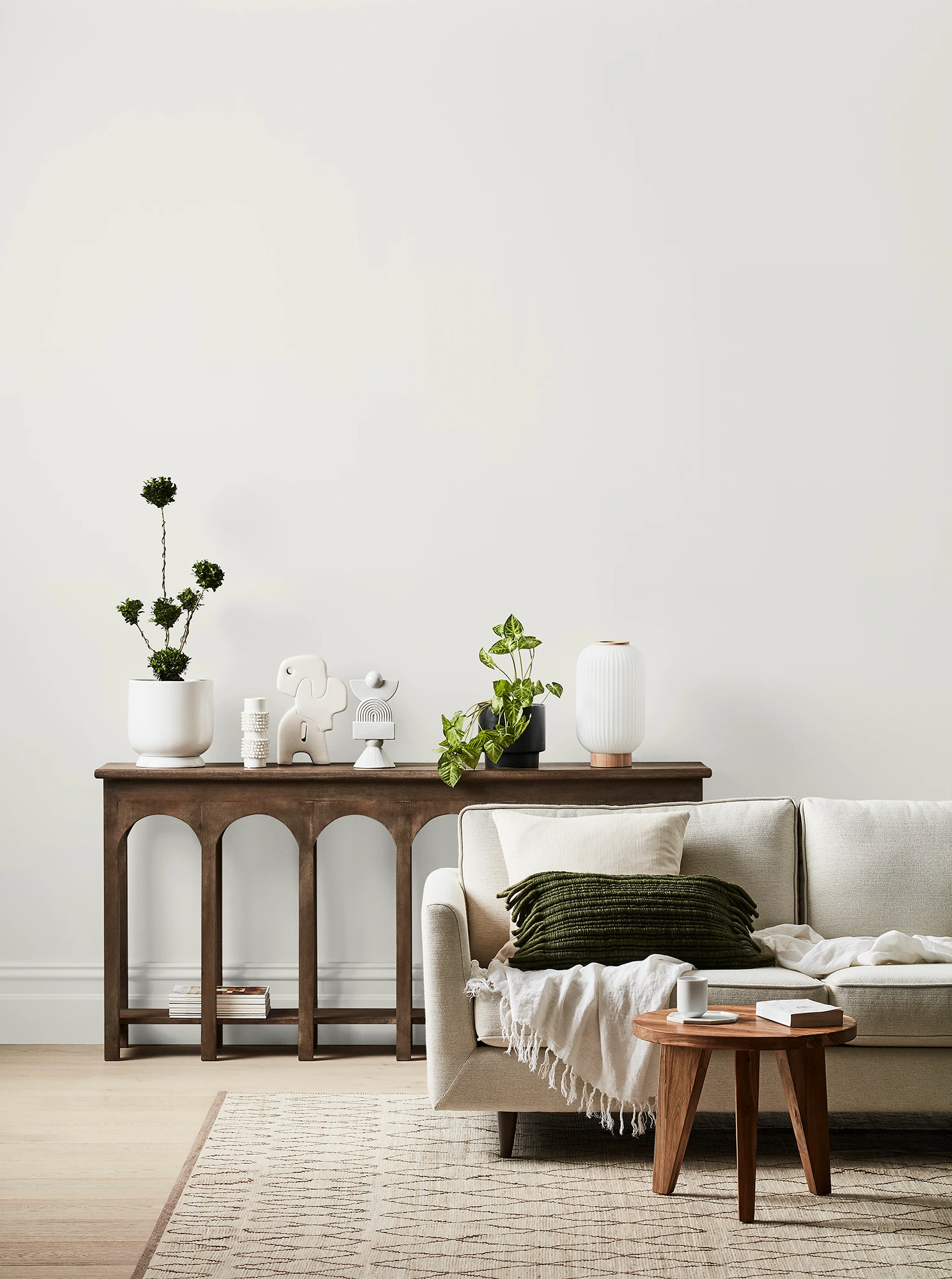 White living room with cream couch, timber side table and timber table with ornaments and plants.