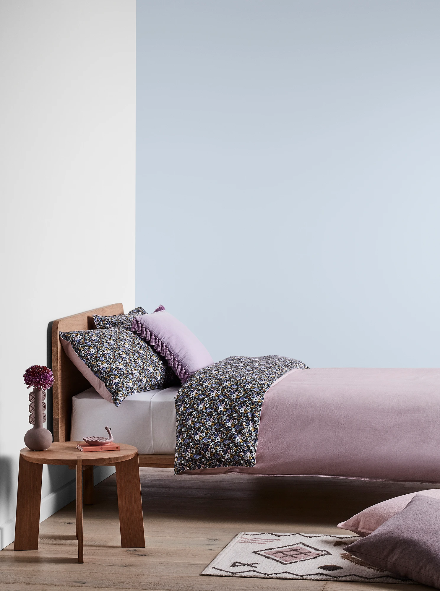 Light purple bedroom with timber bed and side table and purple linens.