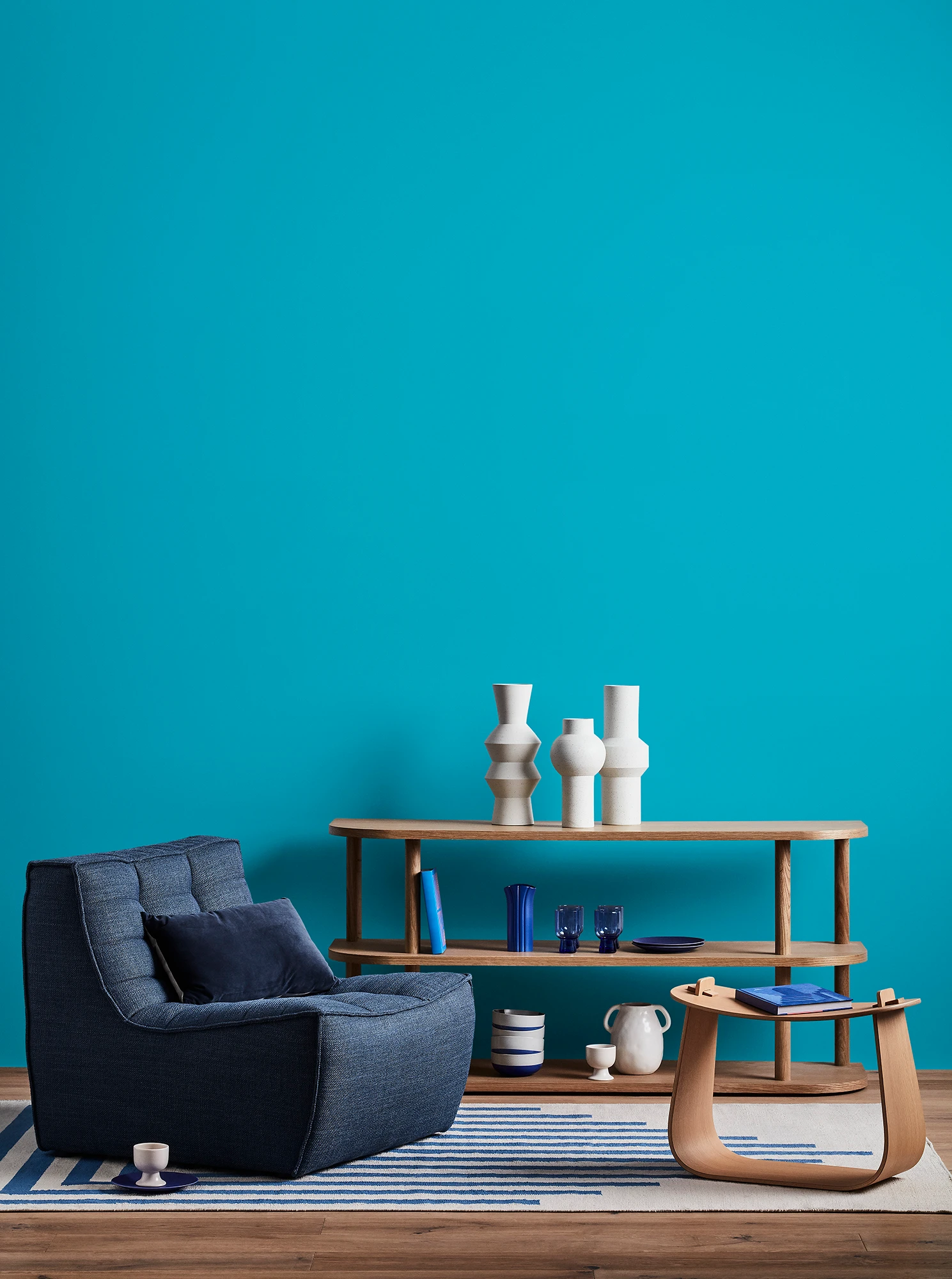 Blue living room with blue armchair, wooden coffee table and shelves with blue and white decor. 