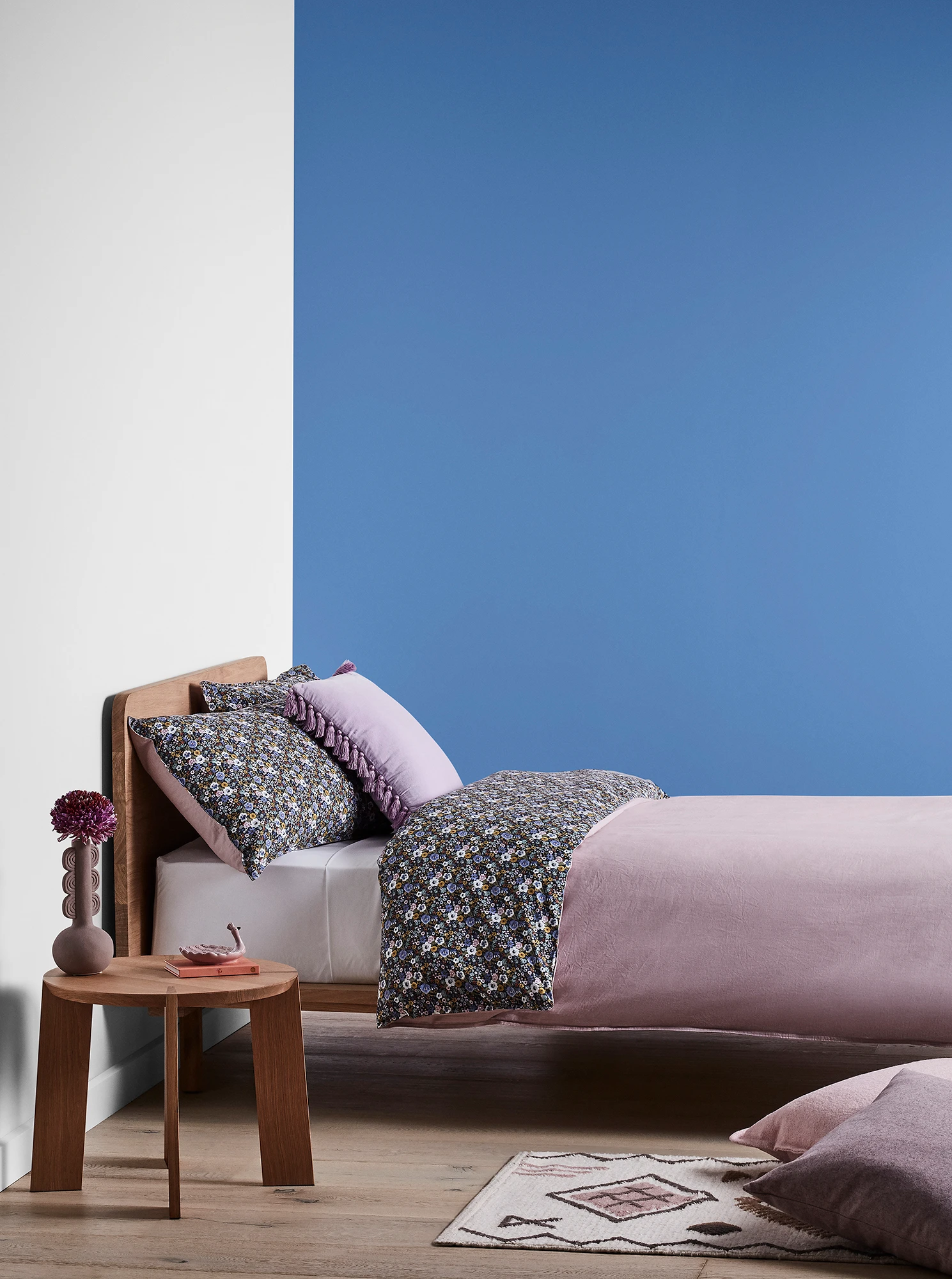 Purple-blue bedroom with timber bed and side table and purple linens.