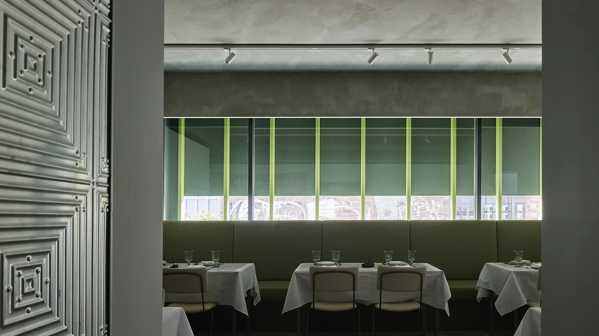 Restaurant with tables with table clothes. Simple downlighting and view of green exterior.