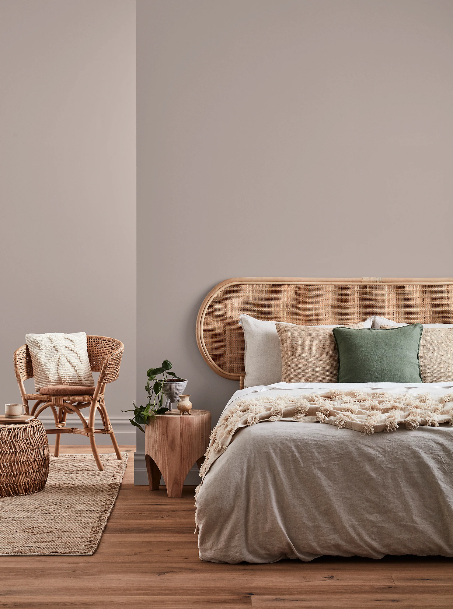 Neutral-coloured bedroom with rattan headboard and chair and neutral linens.