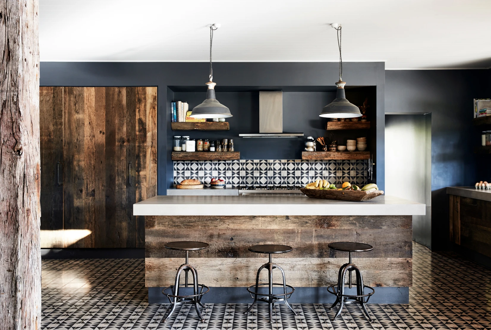 Kitchen and dining area with Domino coloured walls, aged wood cabinets, tiled floors and splash back and concrete look bench tops.