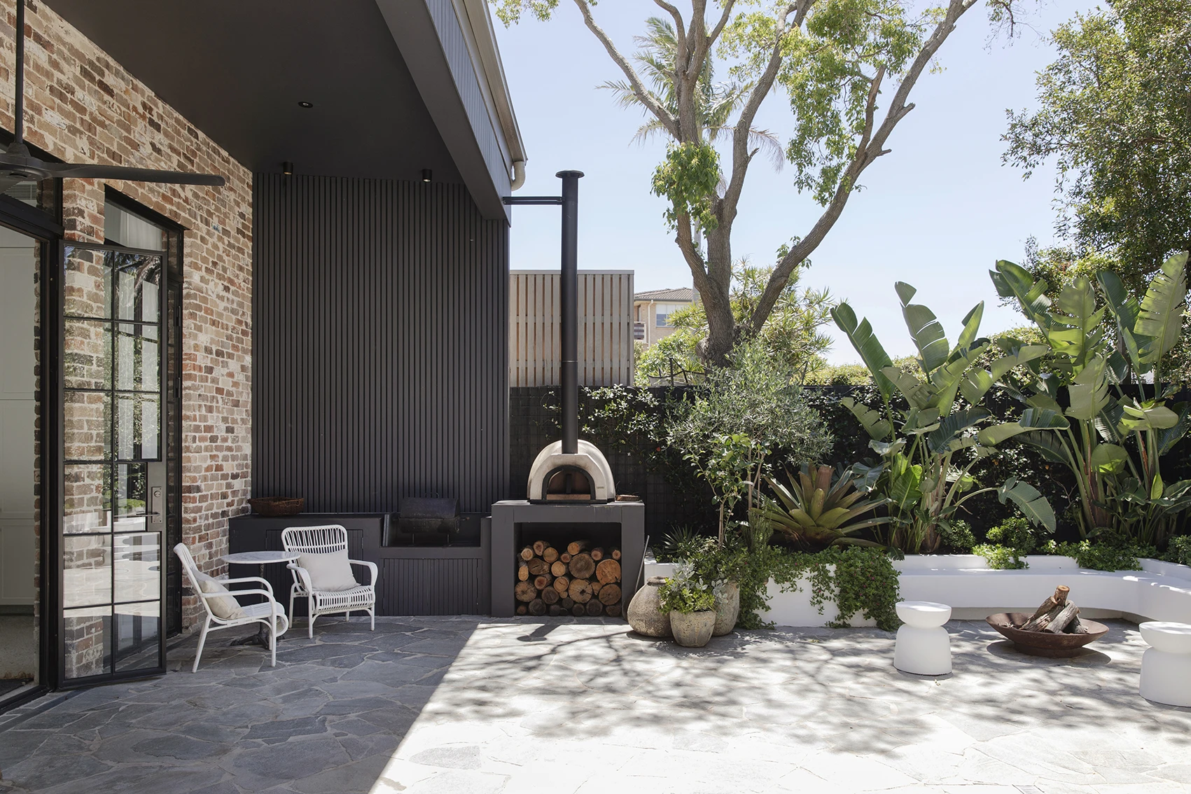 Outdoor entertaining area with wood-fired pizza oven and white wicker chairs.