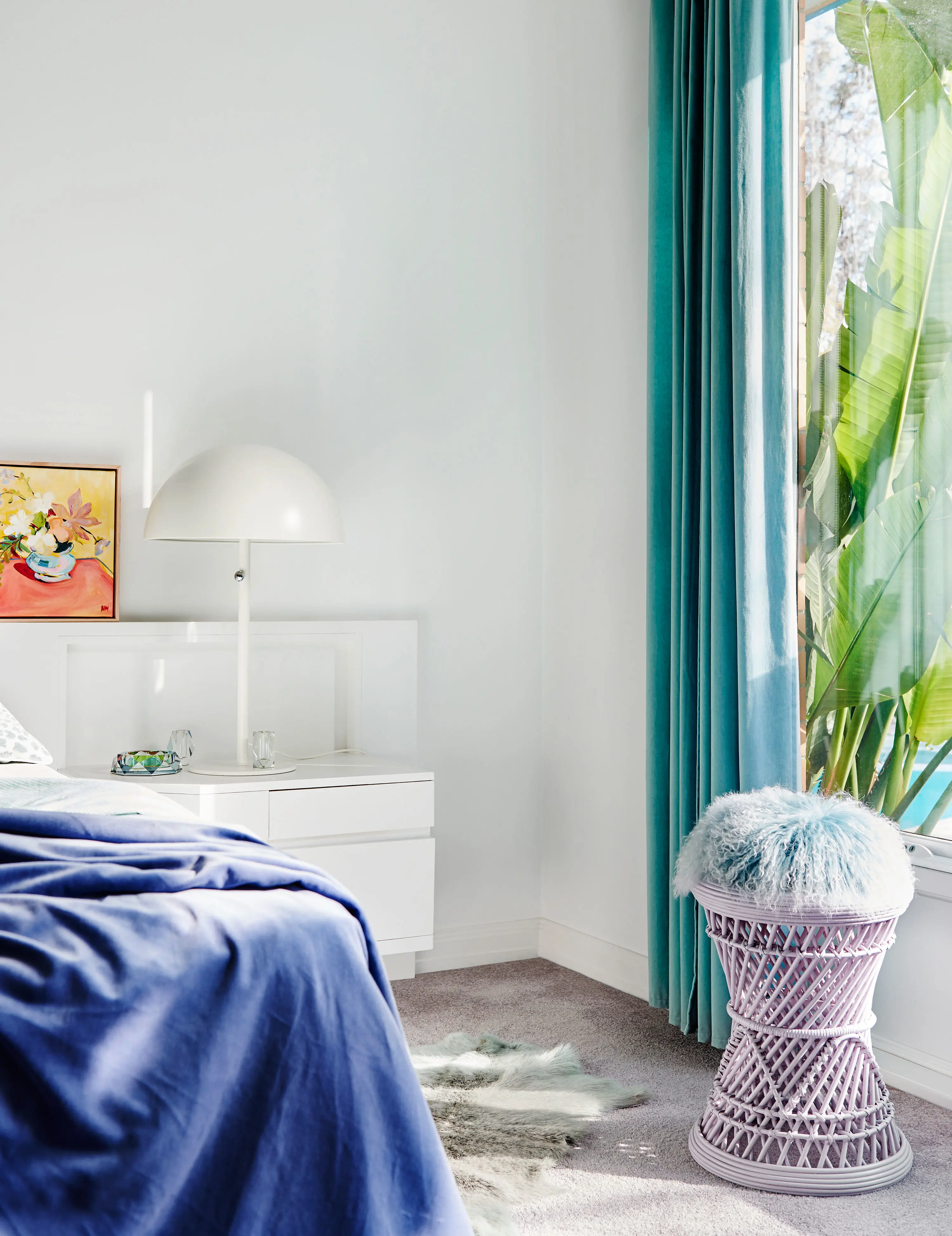 Bedroom with white walls and pops of blue in the curtains and blanket on the bed.