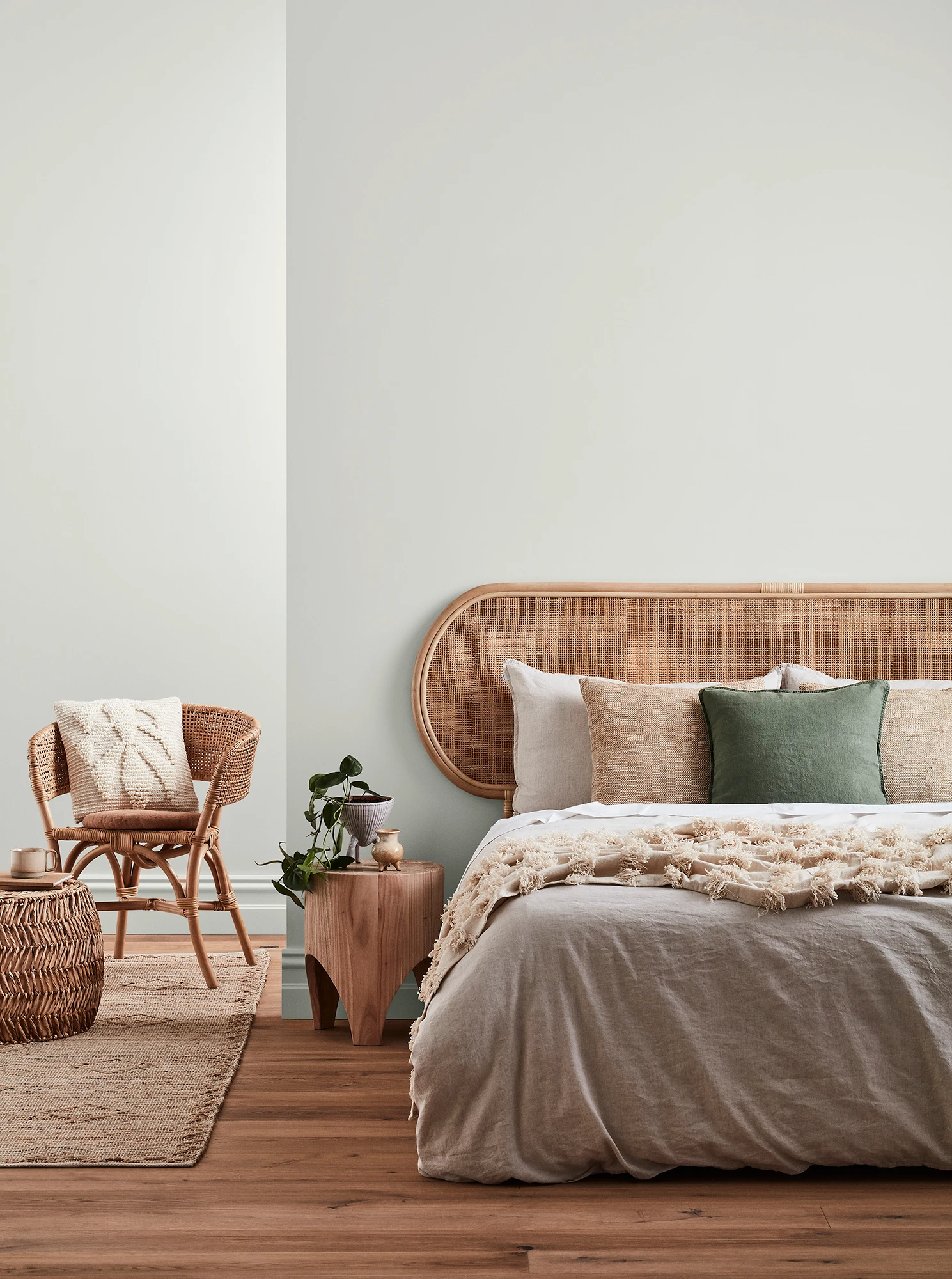 Neutral-coloured bedroom with rattan headboard and chair and neutral linens.