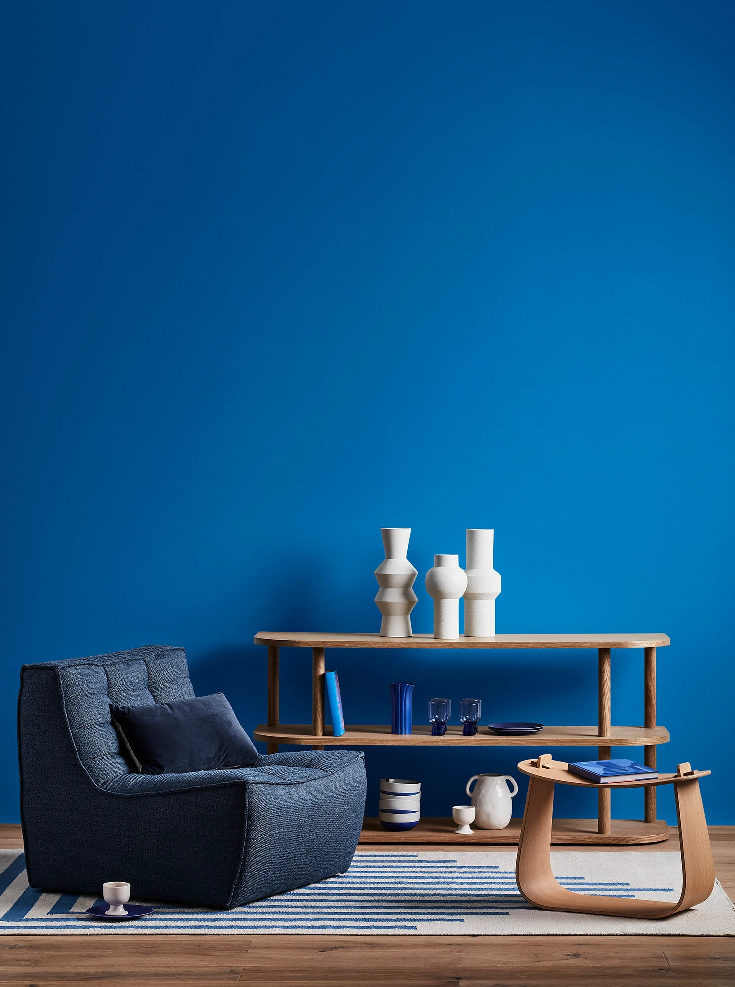 Blue living room with blue armchair, wooden coffee table and shelves with blue and white decor. 