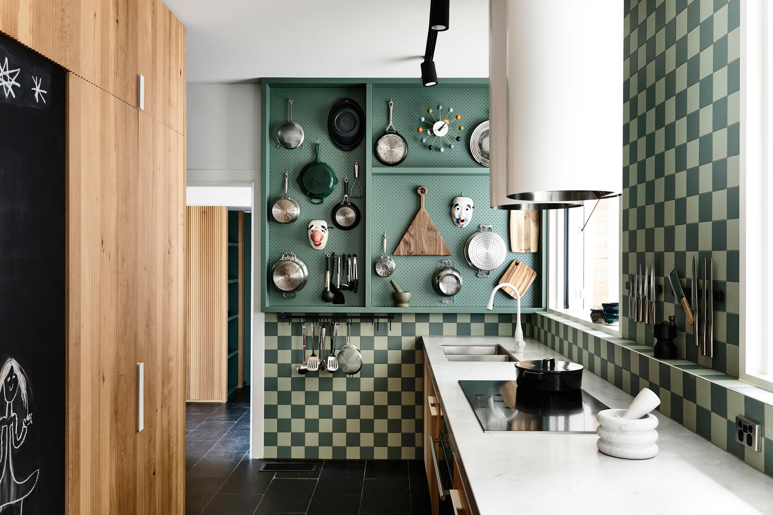kitchen with timber cabiners, light green and dark green square tiles, white bench and frypans displayed on wall