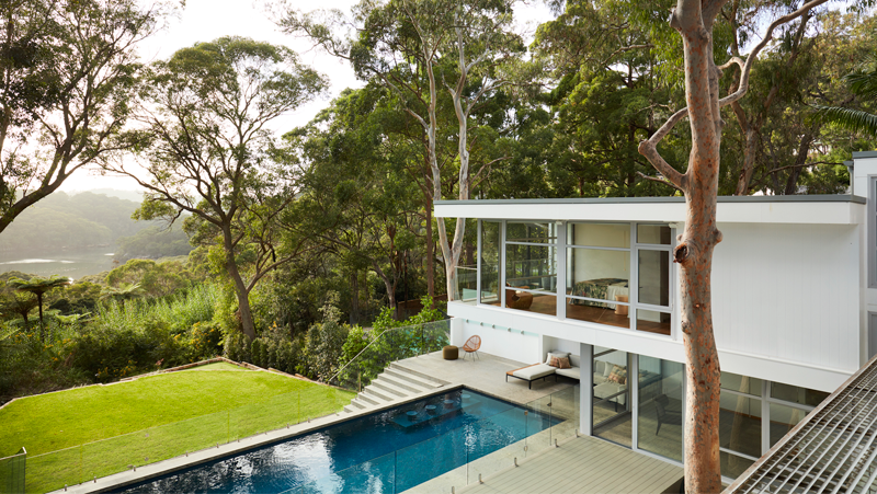 Post-modern white house with a outlook of treed valley, concrete steps and rectangle pool.
