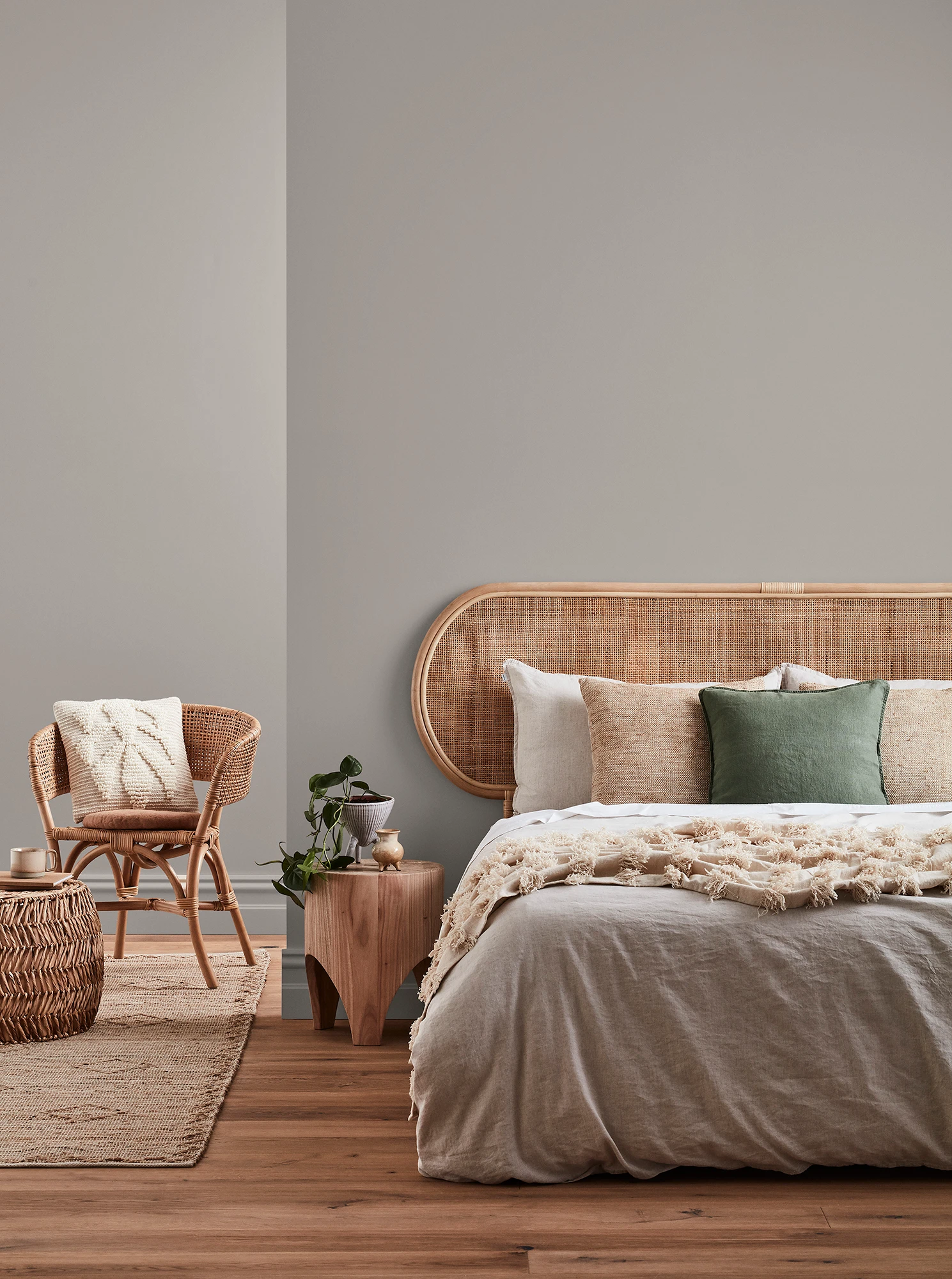 Neutral-coloured bedroom with rattan headboard and chair and neutral linens