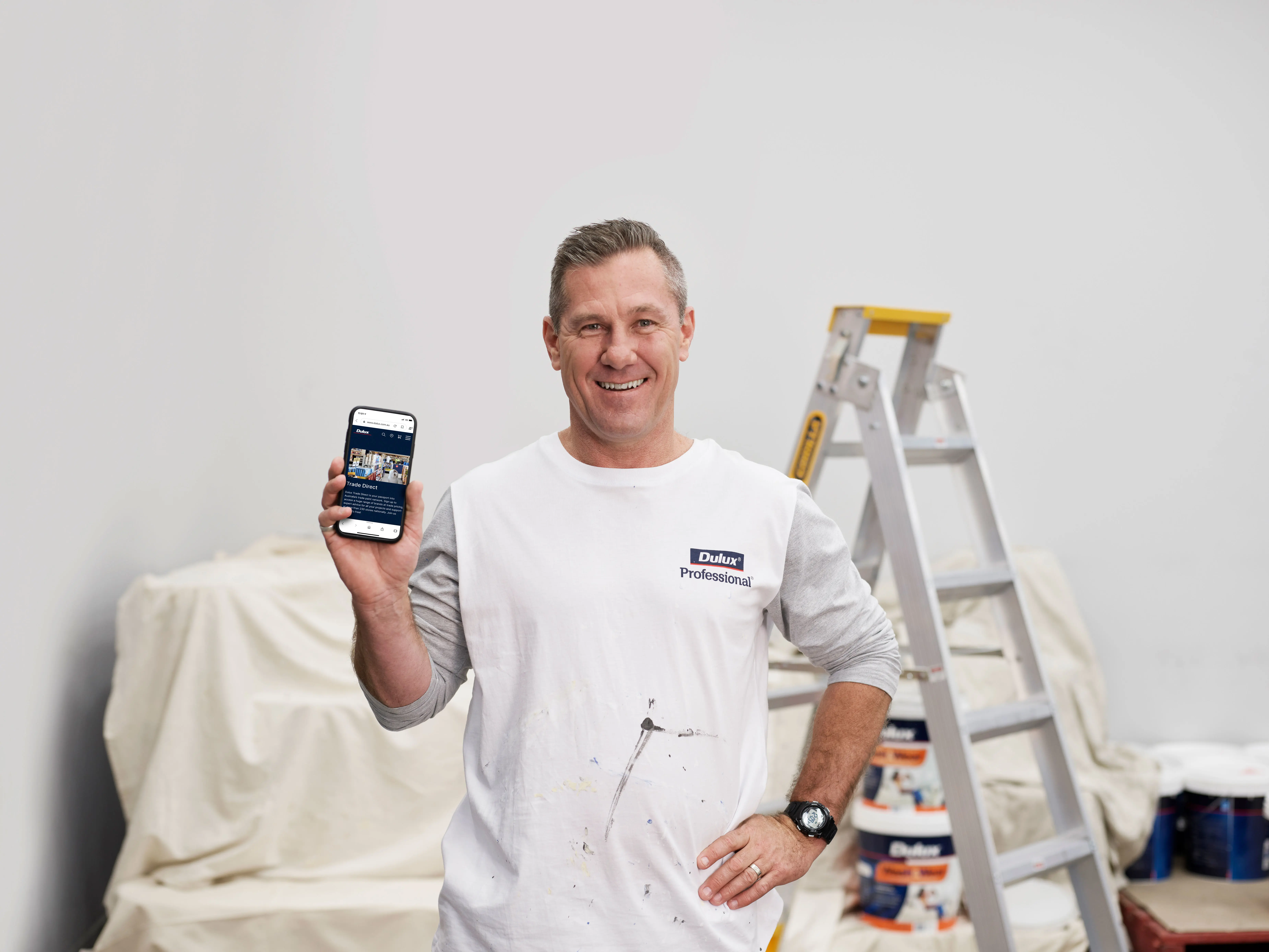 Painter holding smartphone in white room with steel ladder