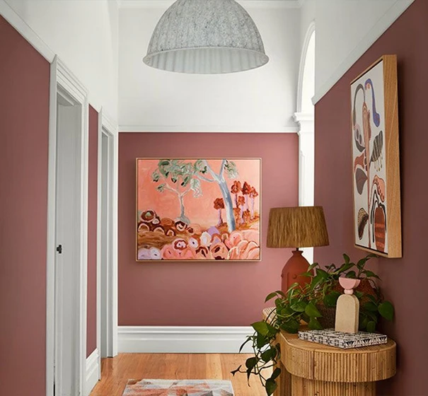 Wide deep pink and white two-tone hallway in traditional home with large artworks on wall and modern hall table with lamp