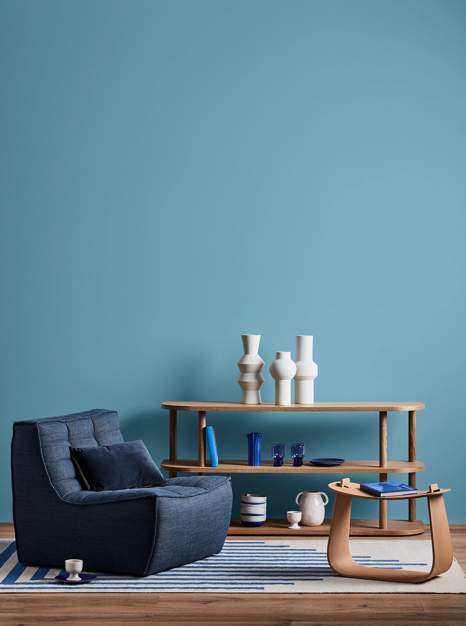 Blue living room with blue armchair, wooden coffee table and shelves with blue and white decor. 