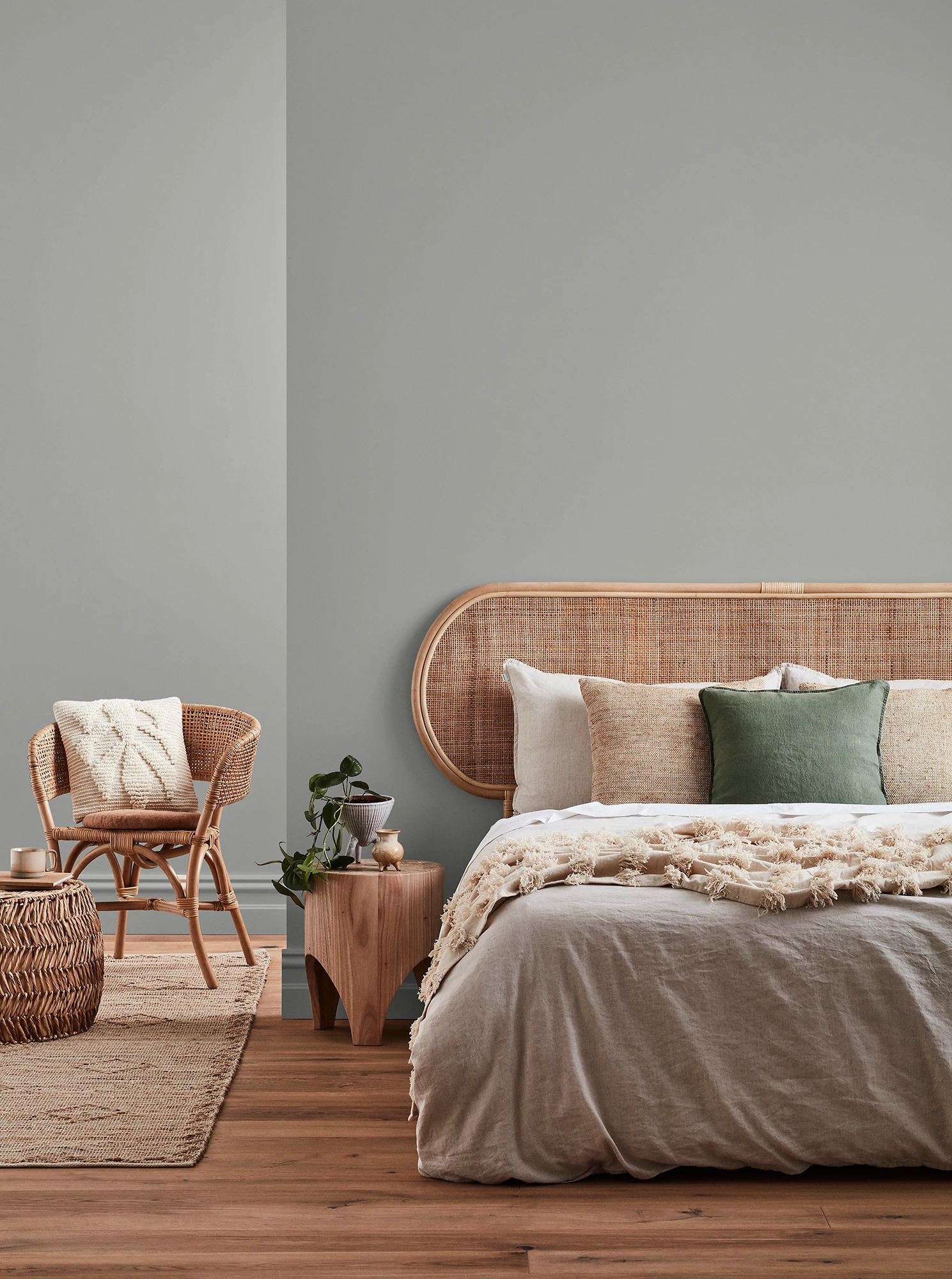 Neutral-coloured bedroom with rattan headboard and chair and neutral linens.