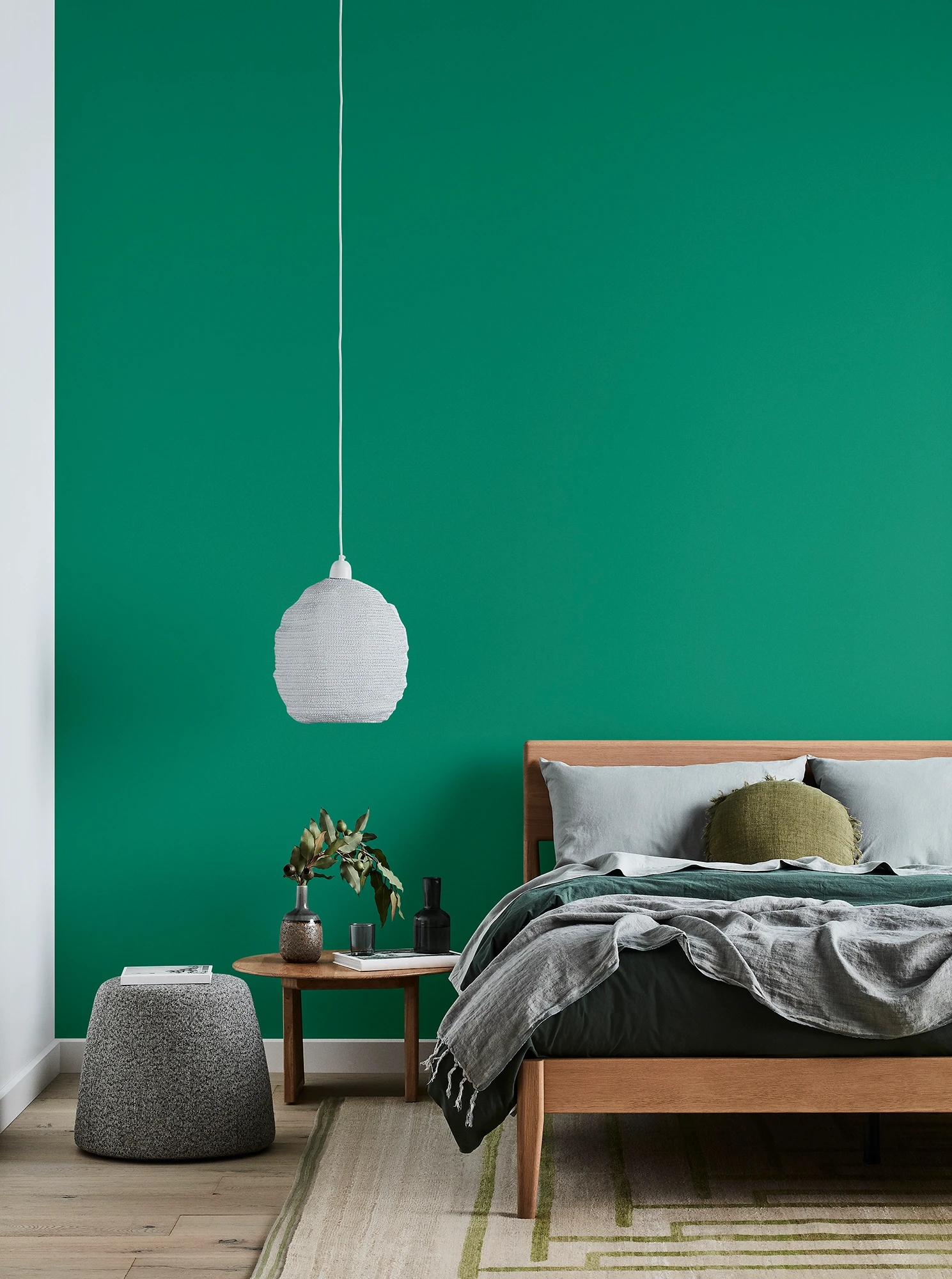 Green bedroom with timber bed and side table, white pendant light and grey linens.