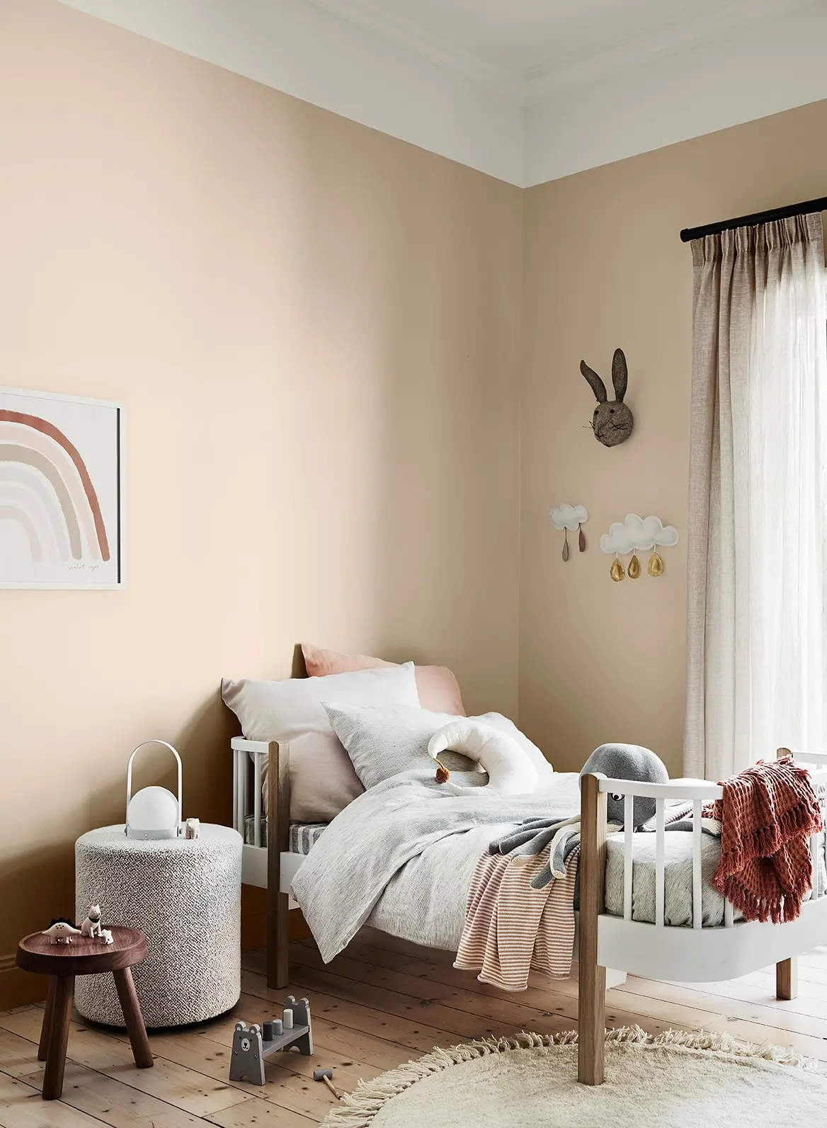 Neutral child's bedroom with a rainbow print on the apricot coloured wall 