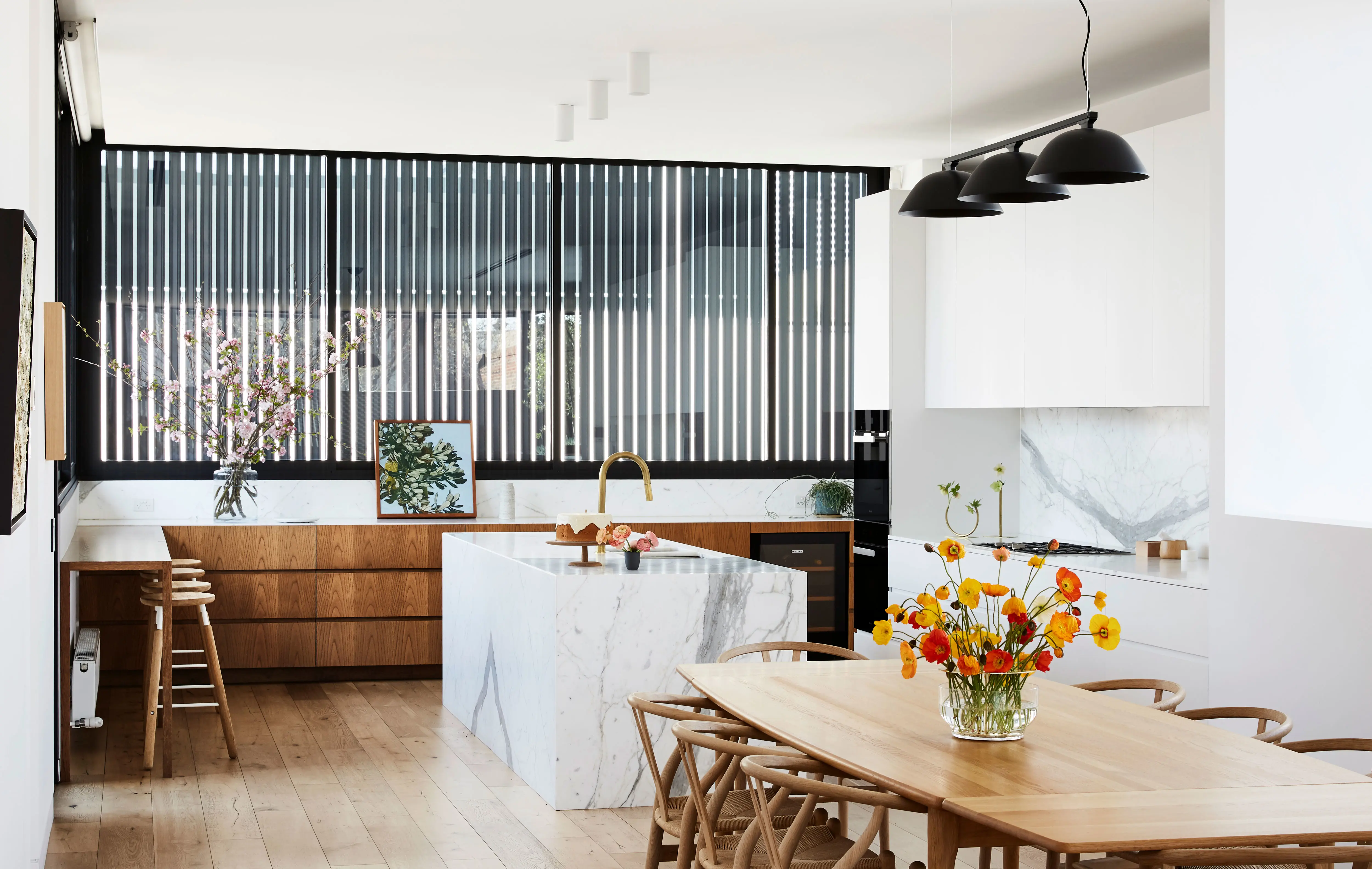 White modern kitchen with black louvres, timber table and marble bench and splashback
