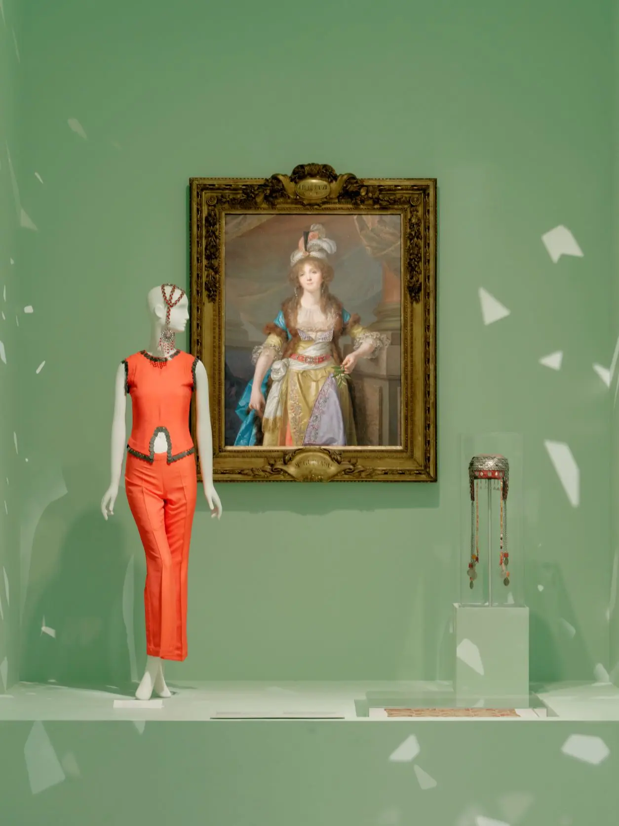 Mannequin wearing orange suit against green background at NGV Alexander McQueen installation