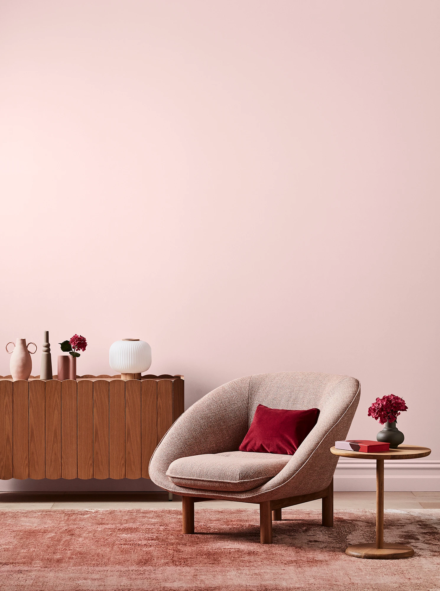 Pink living room with pink armchair, wooden side table and sideboard with white and pink decor.