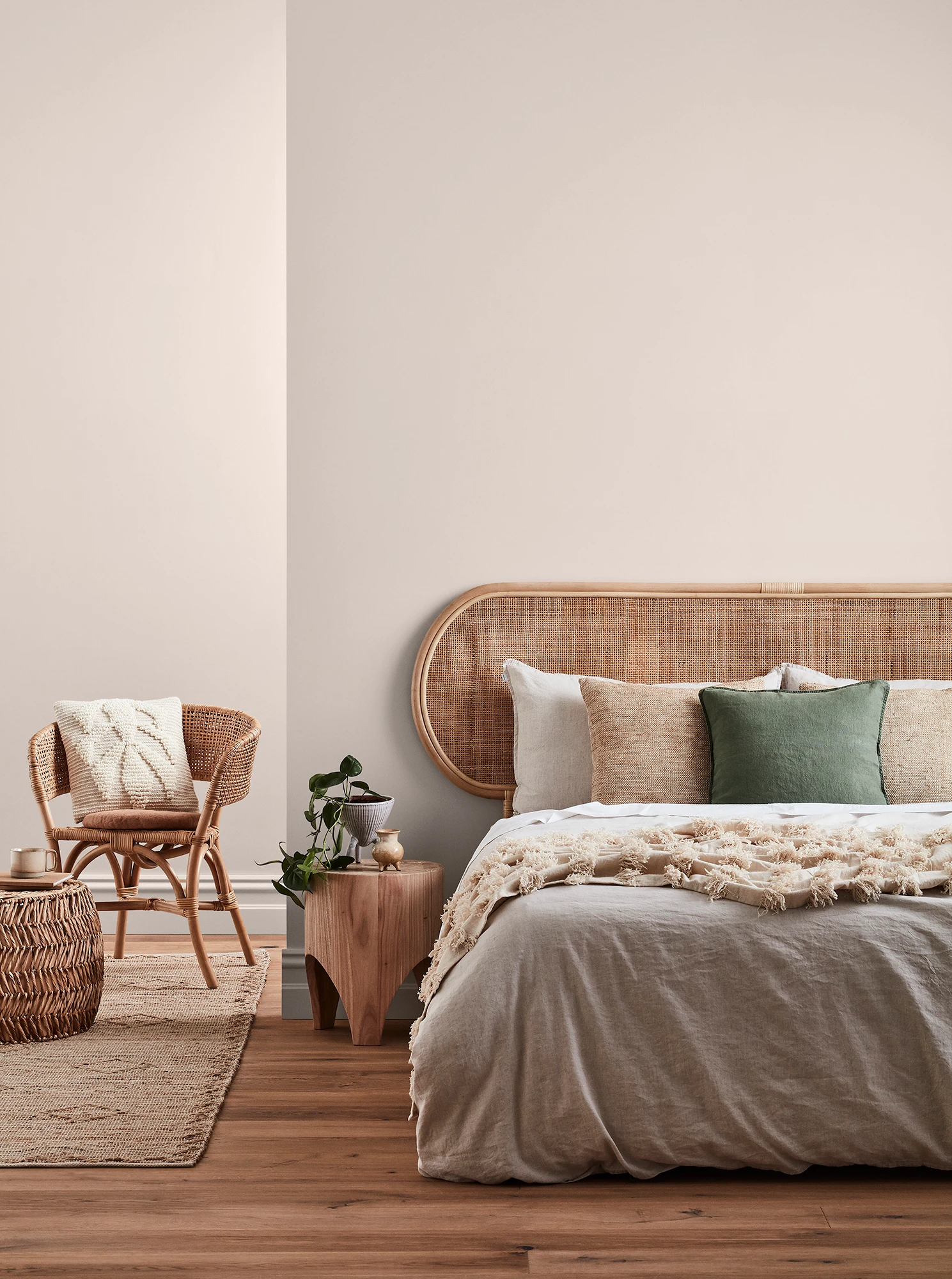 Neutral-coloured bedroom with rattan headboard and chair and neutral linens.