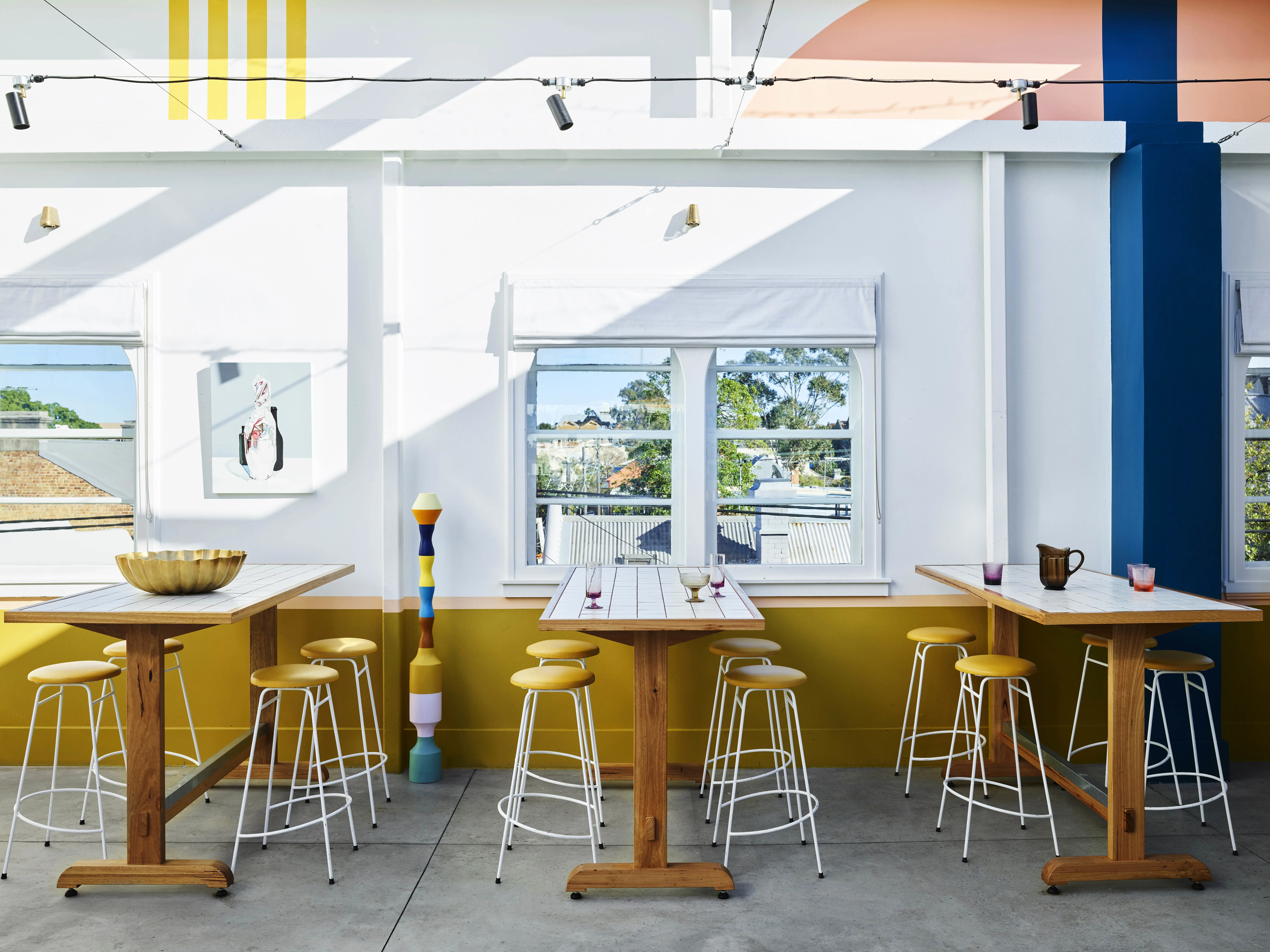 hotel with white and yellow walls, with bar tables and retro metal stools