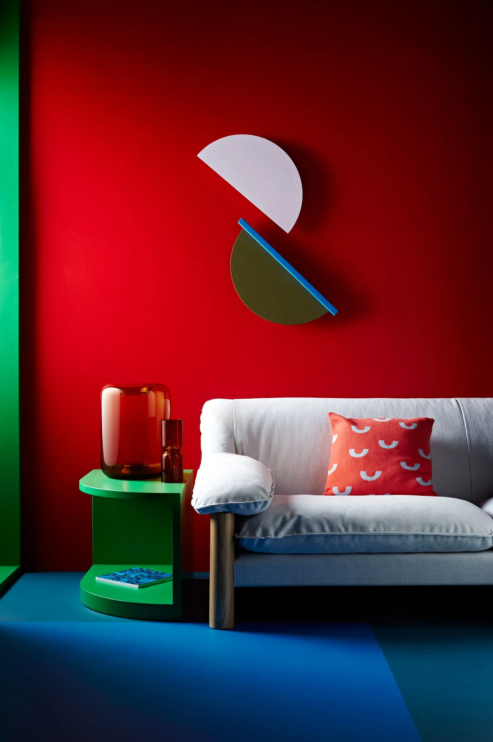 Living room with blue flooring, red wall, semi-circle artwork on wall, white couch and green side table