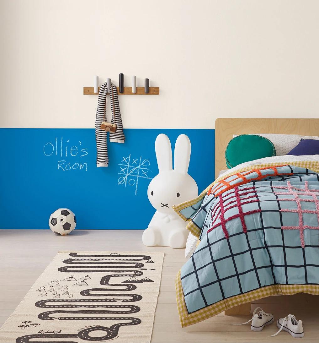 Half blue chalkboard wall and half white wall with children's toys and bed