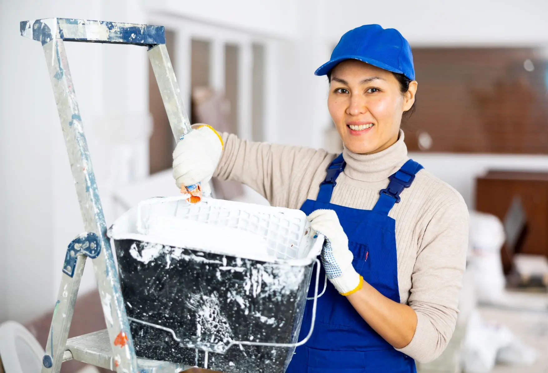Trade painter wearing blue cap and overalls painting community building interior