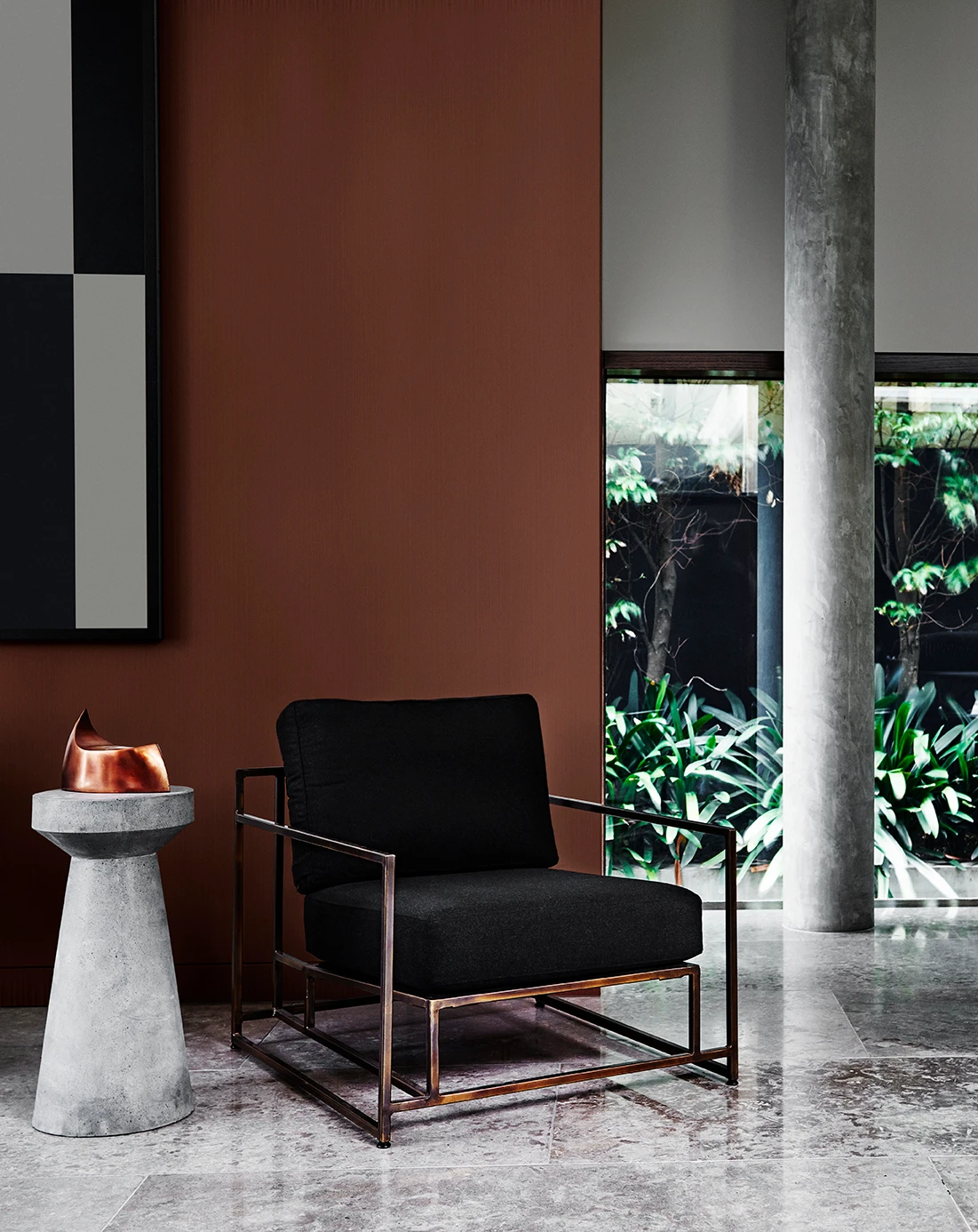 living room with metal armchair with black cushions, polished concrete floors, concrete column and side table. Grey wall and brown wall.