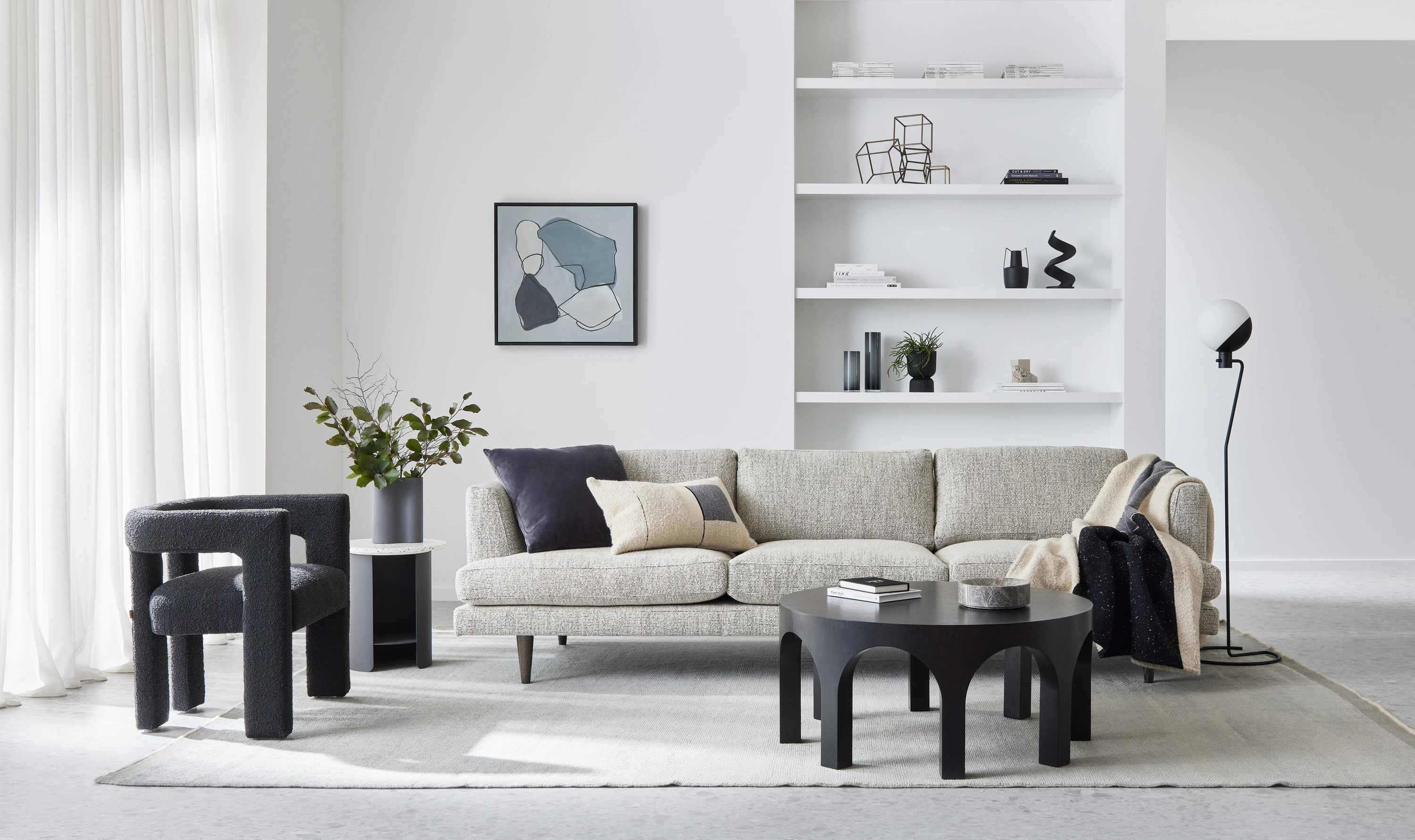 Living area with lounge, coffee table, side chair, side tables and lamp. Wall shelves in background.