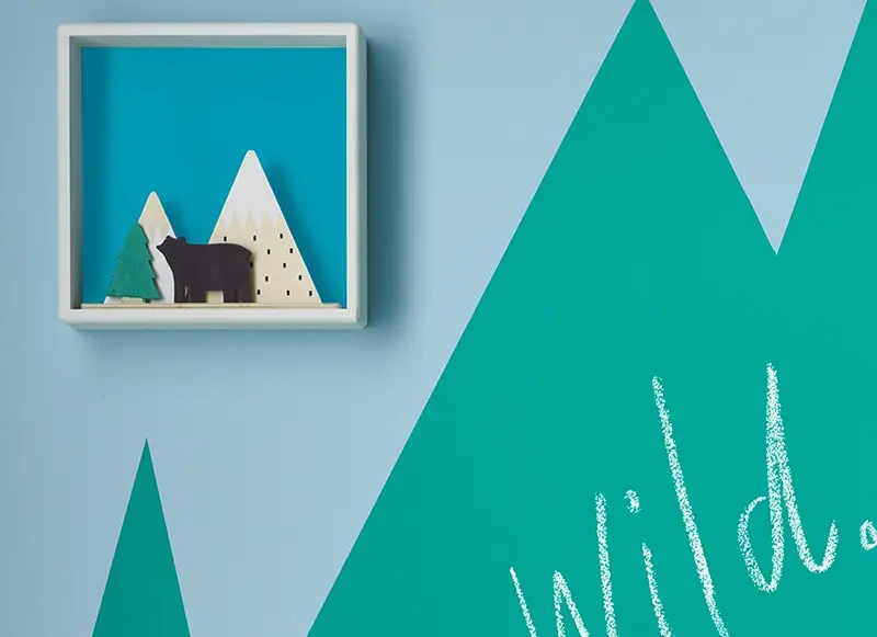 A blue wall with green mountain shapes painted on in chalkboard paint