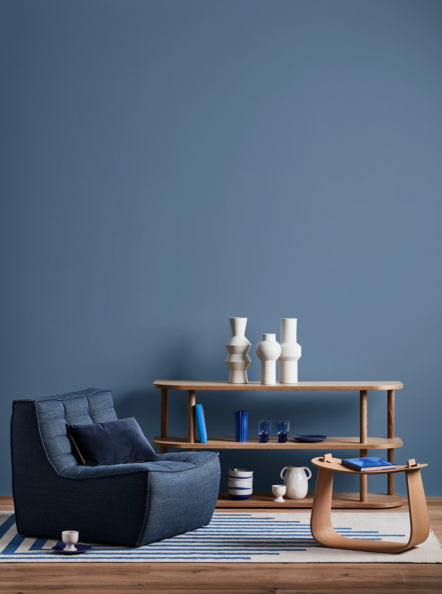 Blue living room with blue armchair, wooden coffee table and shelves with blue and white decor. 