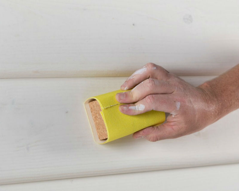 Persons hand sanding paint weatherboards