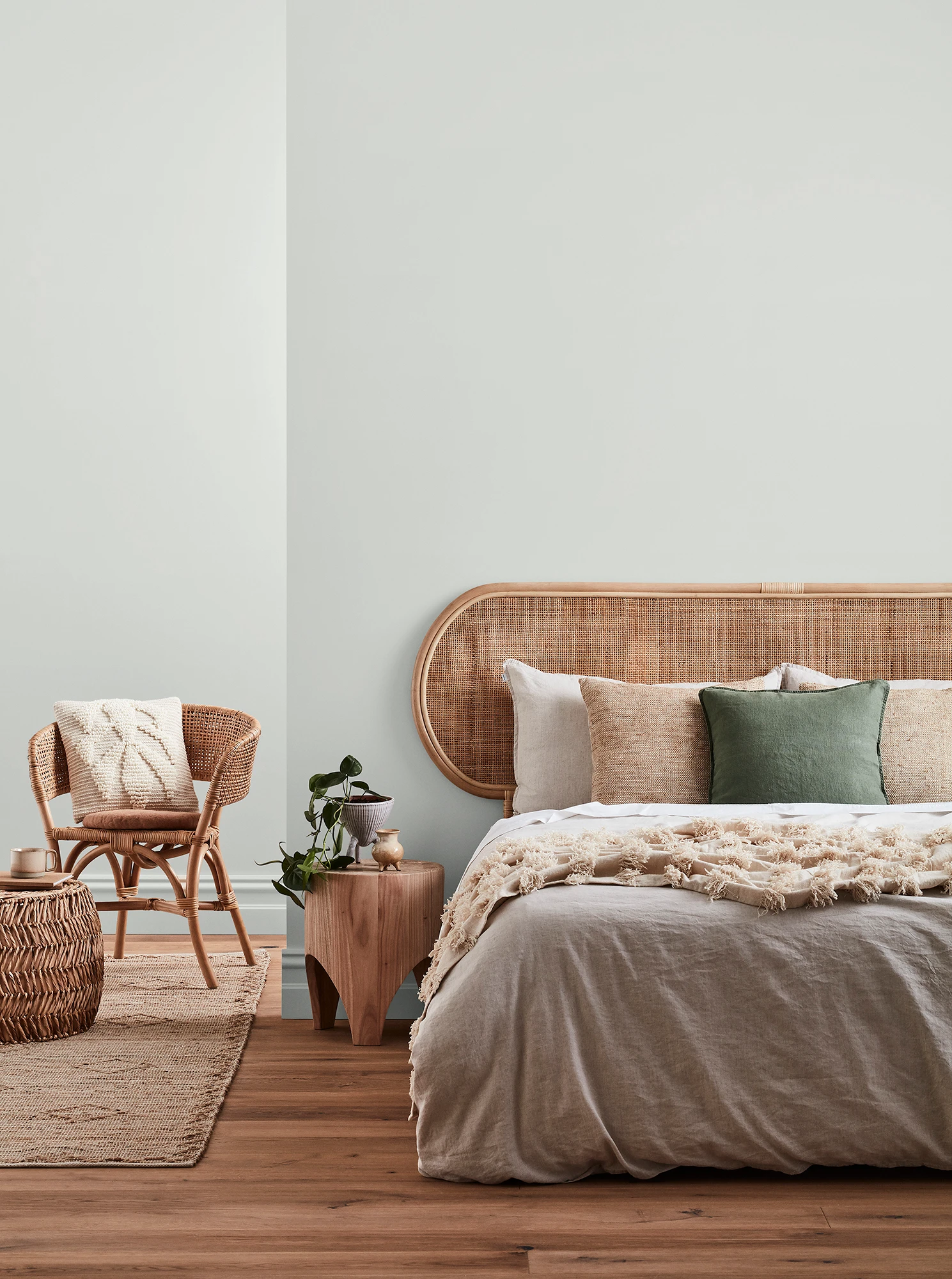 Soft neutral grey-white-coloured bedroom with rattan headboard and chair and neutral linens.