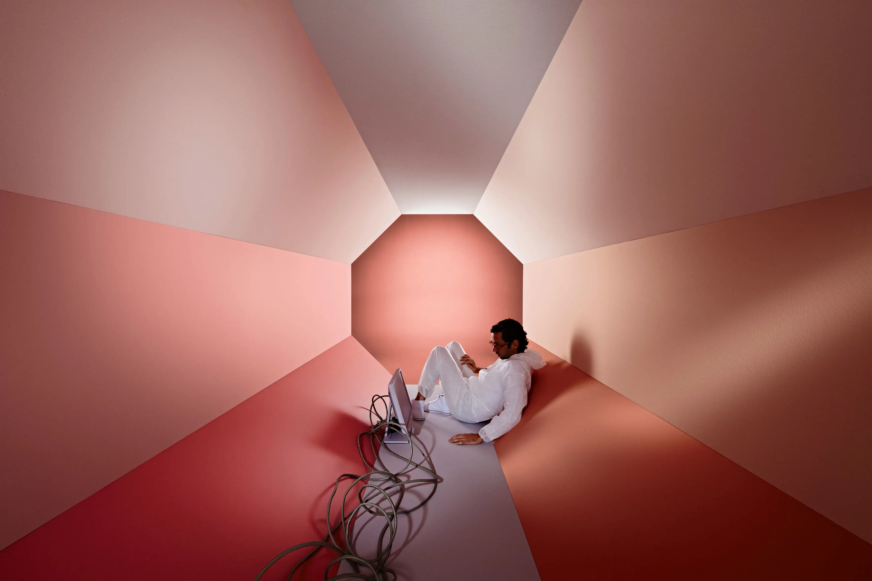 Man in peach-coloured hexagon tube with computer