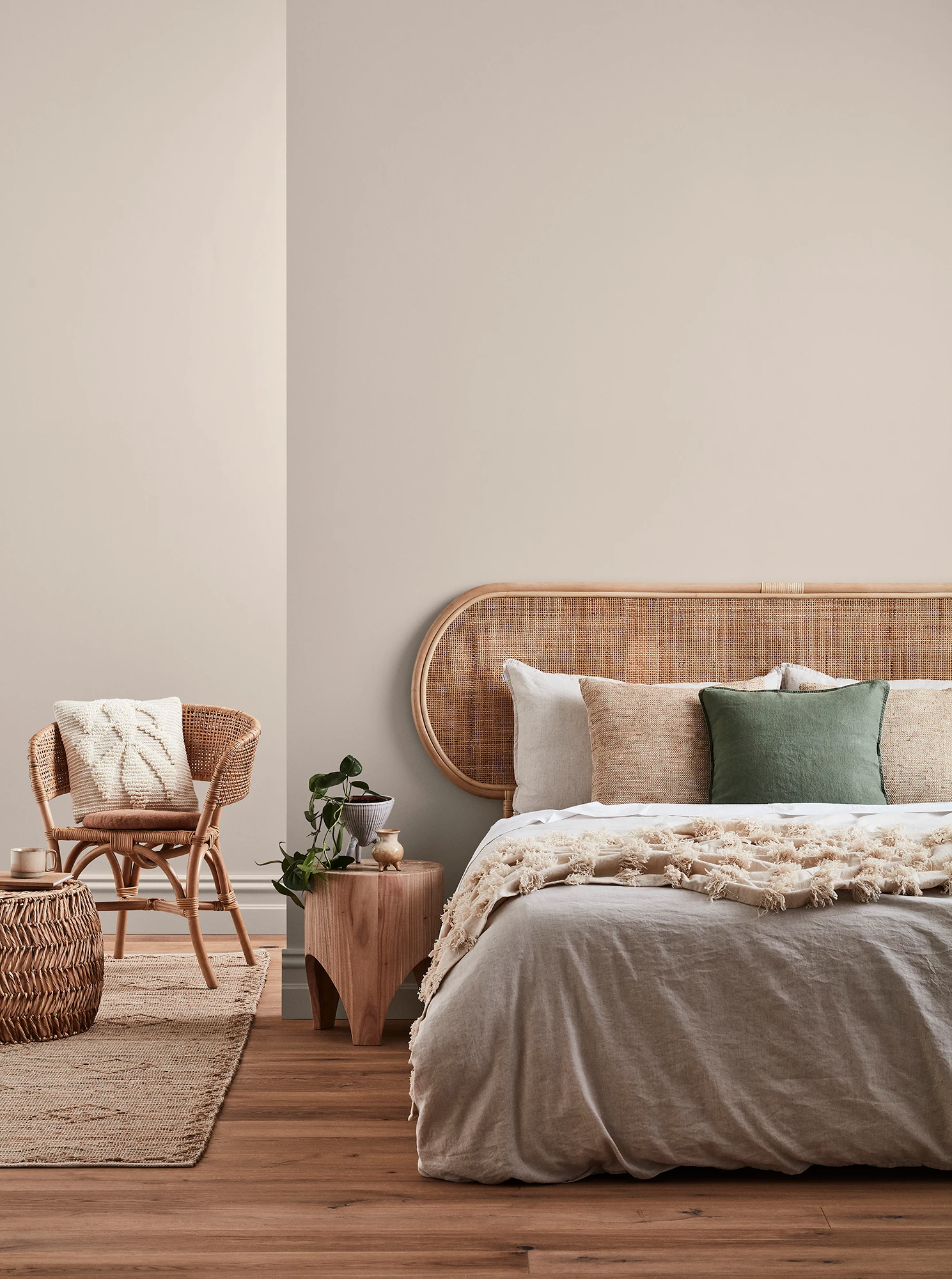 Neutral-coloured bedroom with rattan headboard and chair and neutral linens.