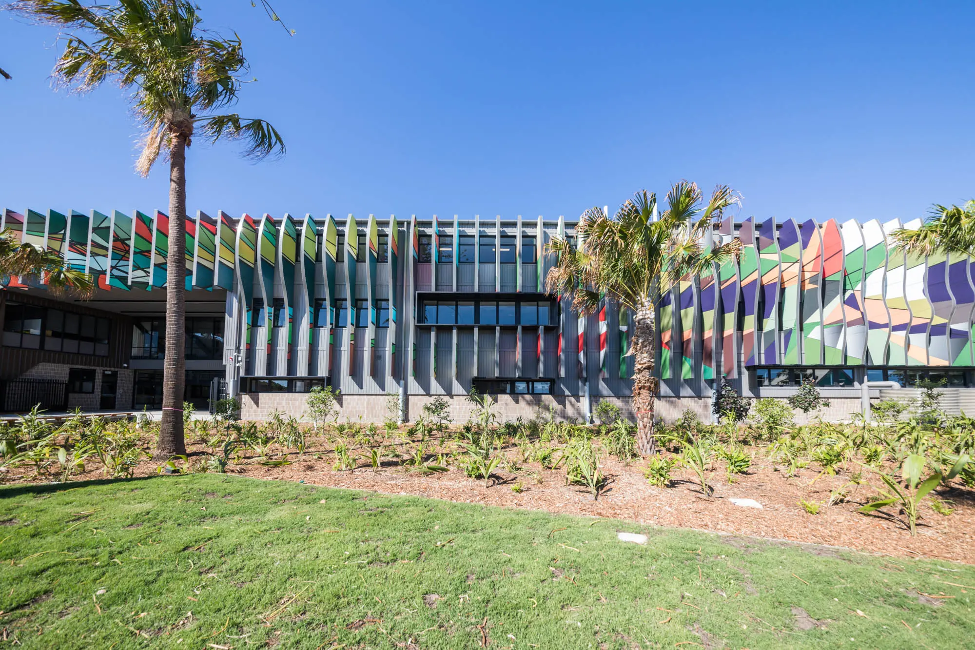 Exterior school building with multi-coloured louvres. Palm trees in the foreground.