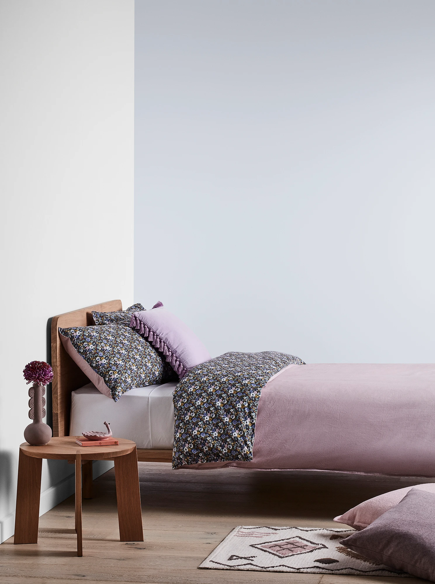 Light blue bedroom with timber bed and side table and purple linens.