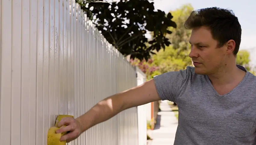 man wiping down picket fence